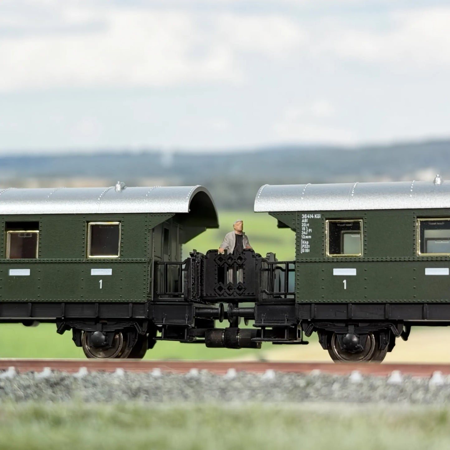 Klassische Übergangsbrücke zwischen zwei Fleischmann Donnerbüchsen (Länderbahnwagen). Auf dem Übergang steht ein reisender Mann.