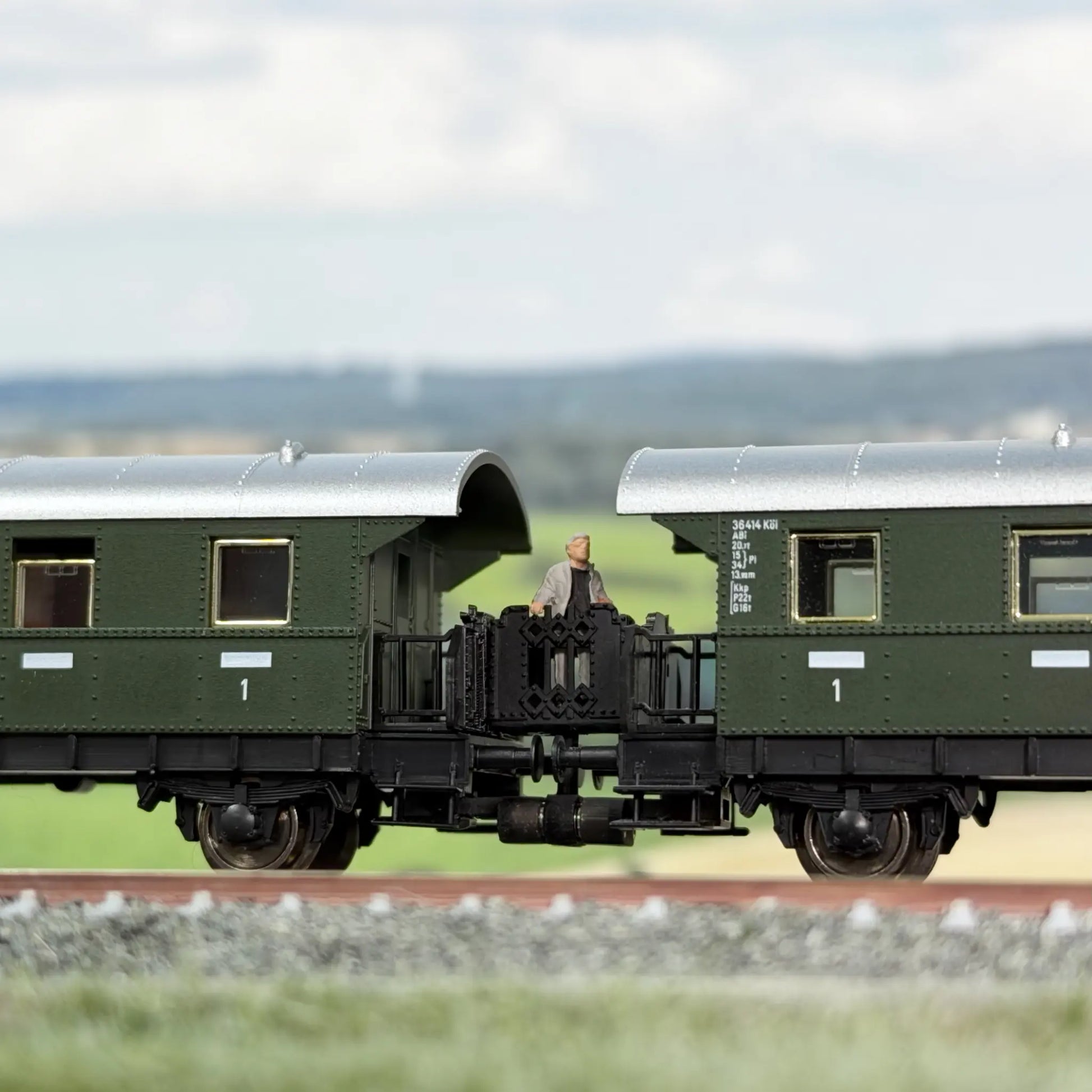 Klassische Übergangsbrücke zwischen zwei Fleischmann Donnerbüchsen (Länderbahnwagen). Auf dem Übergang steht ein reisender Mann.