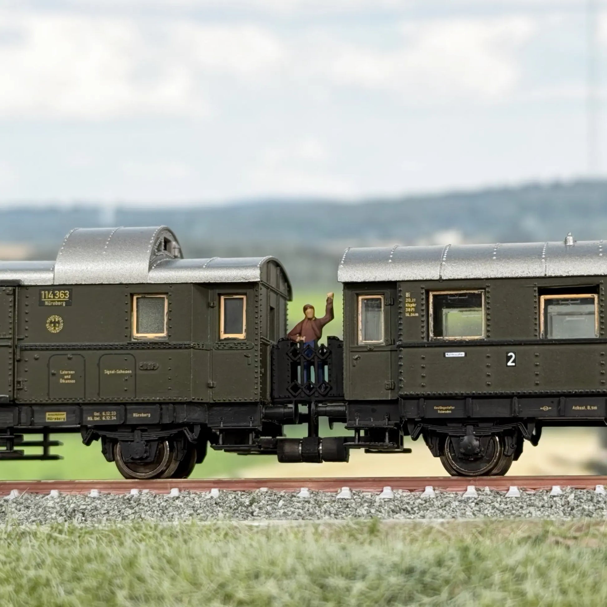 Verbindung zwischen zwei Fleischmann Donnerbüchsen (Länderbahnwagen), einem Bi Wagen und einem Pwi Gepäckwagen. Auf der Übergangsbrücke steht ein reisender Mann, er winkt