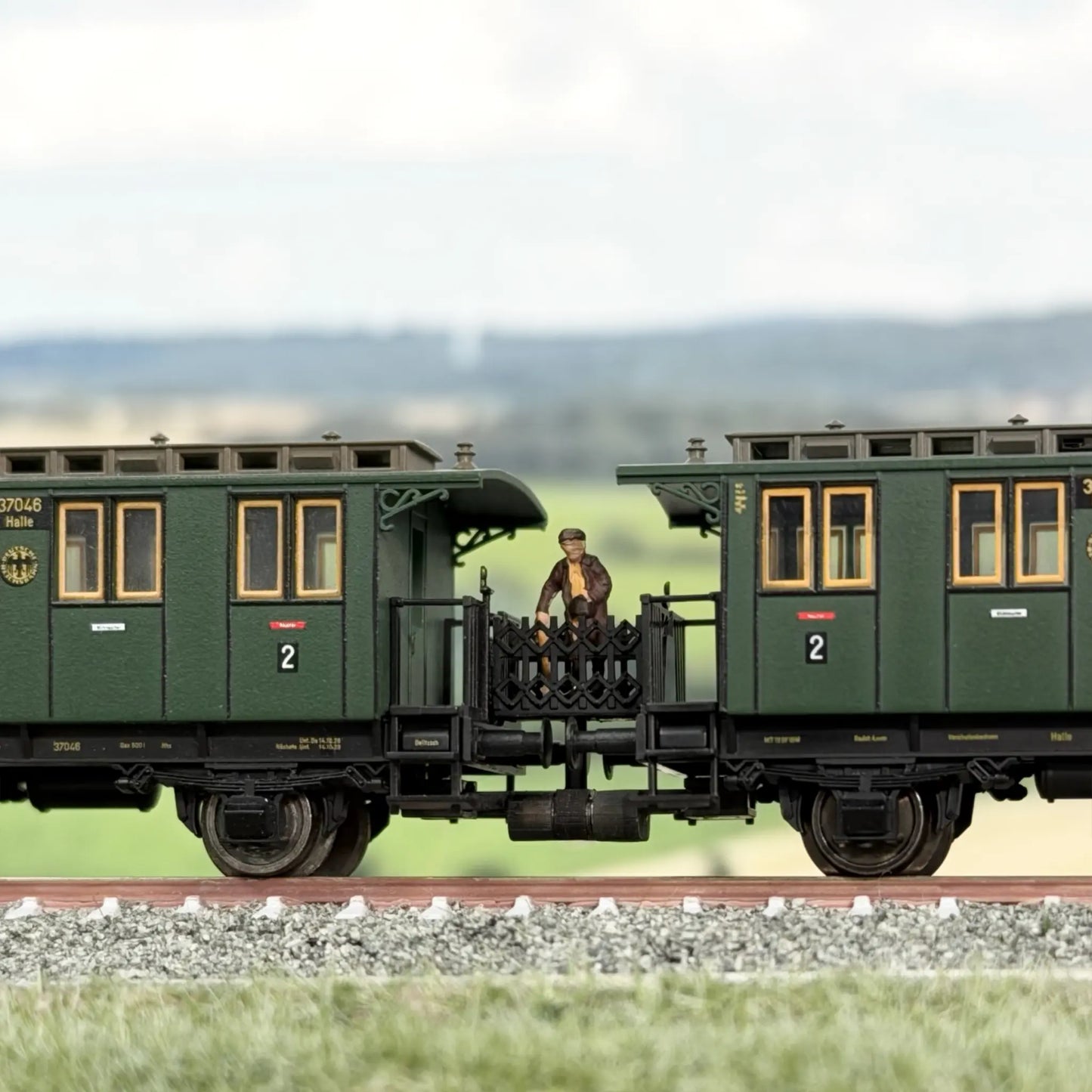 Scherengitter Verbindung zwischen zwei Fleischmann Länderbahnwagen (Donnerbüchsen), darauf steht eine Frauen-Figur mit einer Reisetasche von Preiser.